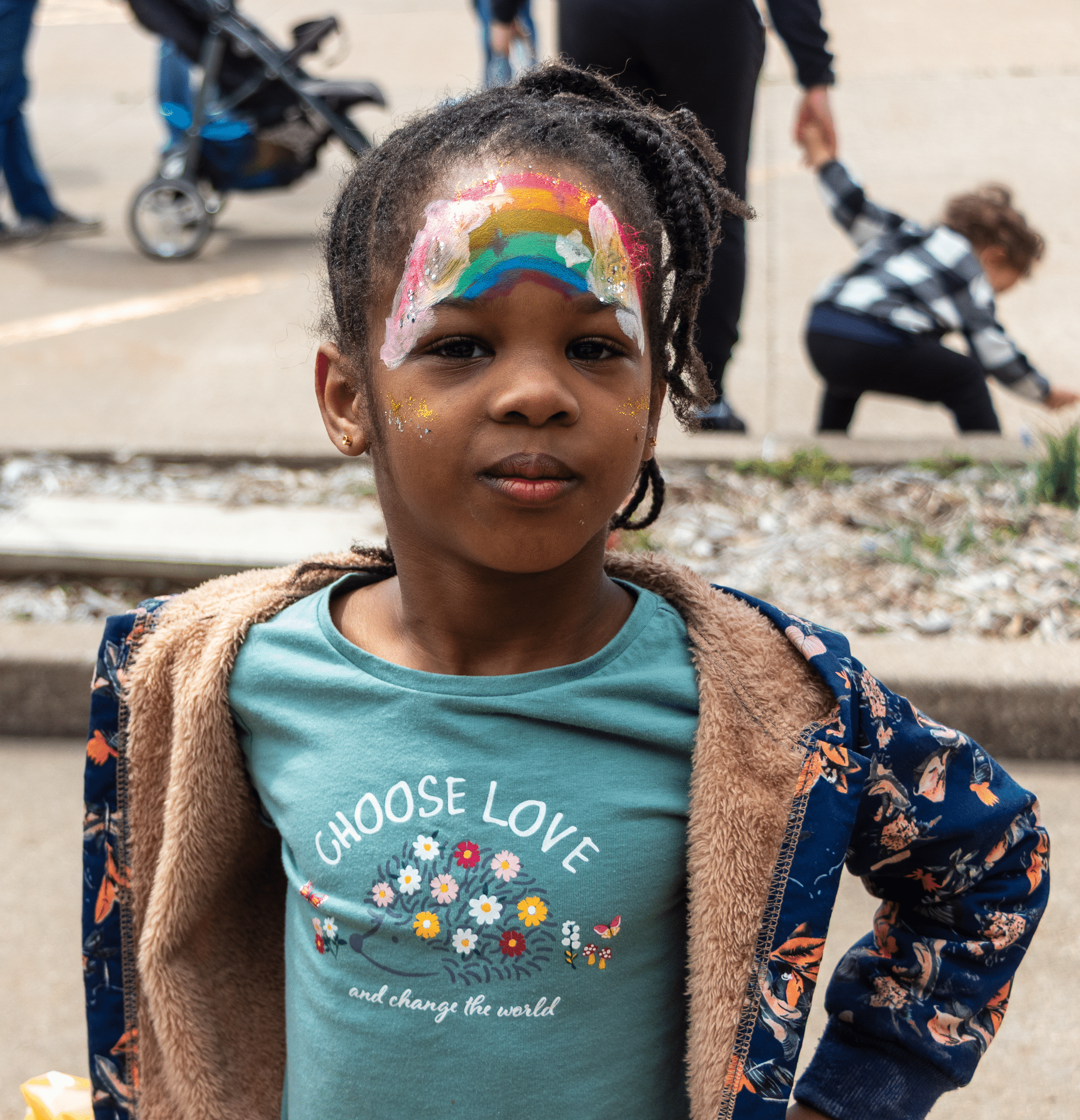 A joyful girl with a rainbow on her forehead wears a Choose Love shirt, surrounded by our welcoming church family. - Muscatine Church of Christ