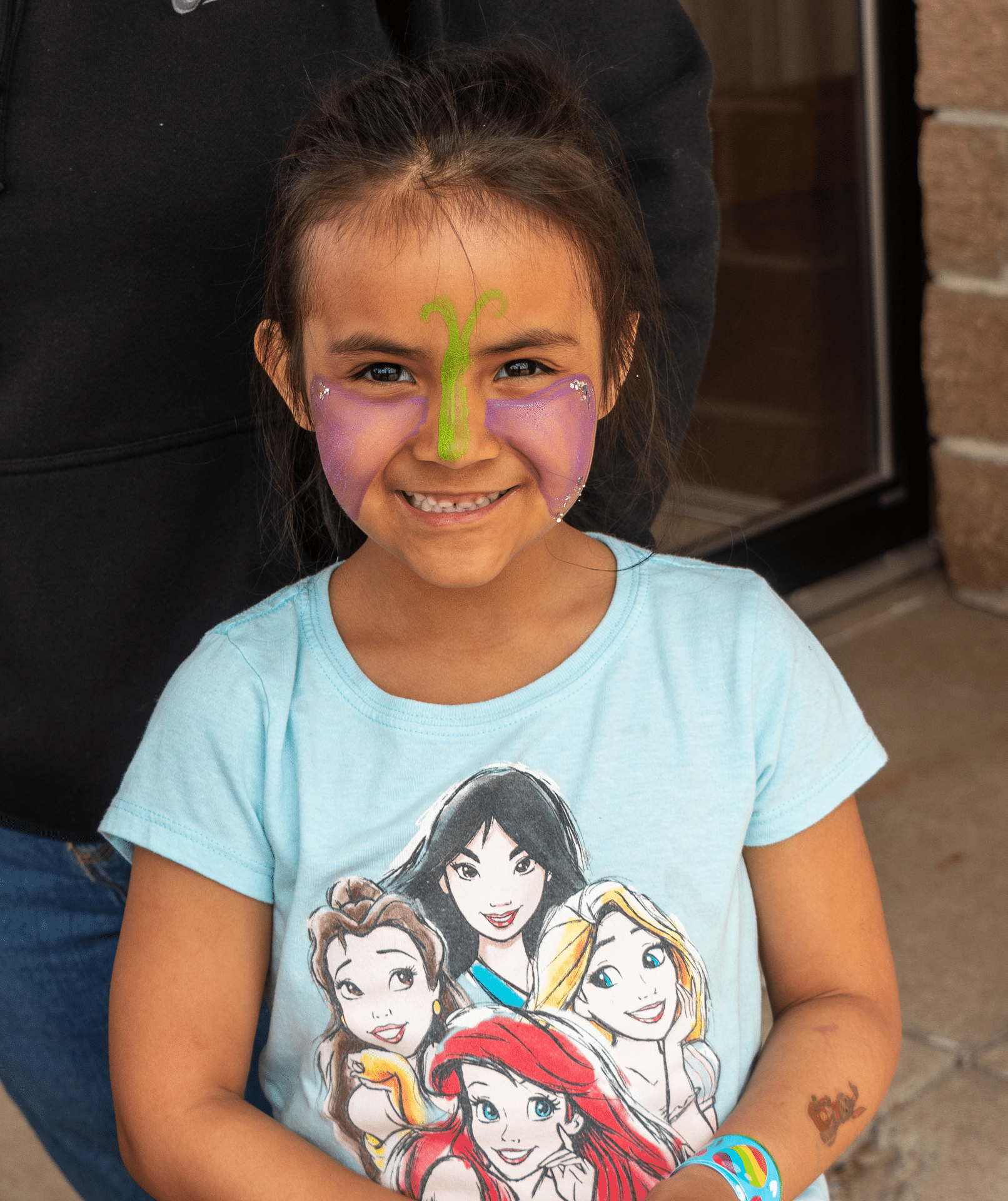 Smiling young girl with colorful face paint welcomes you outside our church—a place of community, joy, and hope. - Muscatine Church of Christ