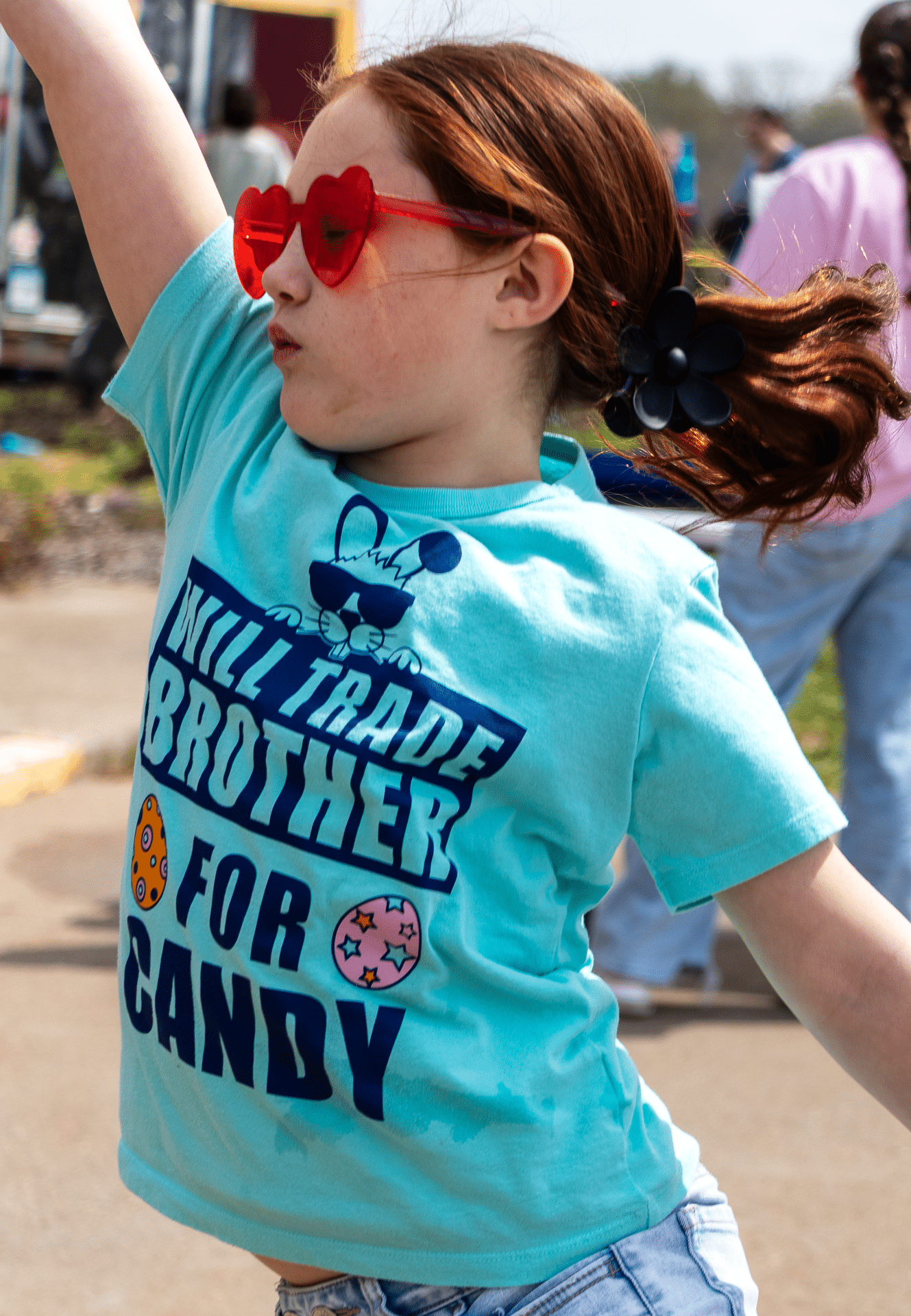 Smiling girl in heart sunglasses outside, reaching up with joy—everyone is welcome in our caring community. - Muscatine Church of Christ