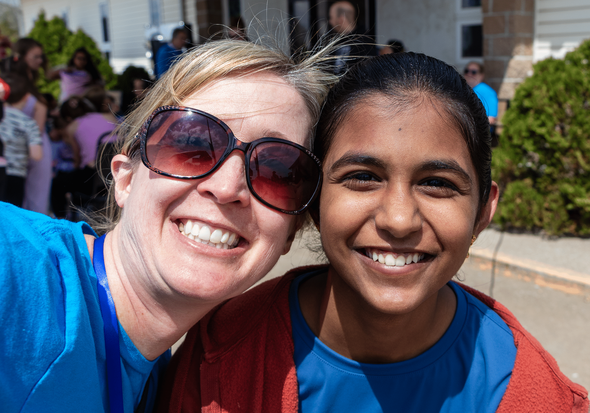 Two women share a joyful moment outdoors, surrounded by friends and nature—a warm welcome from our church family. - Muscatine Church of Christ