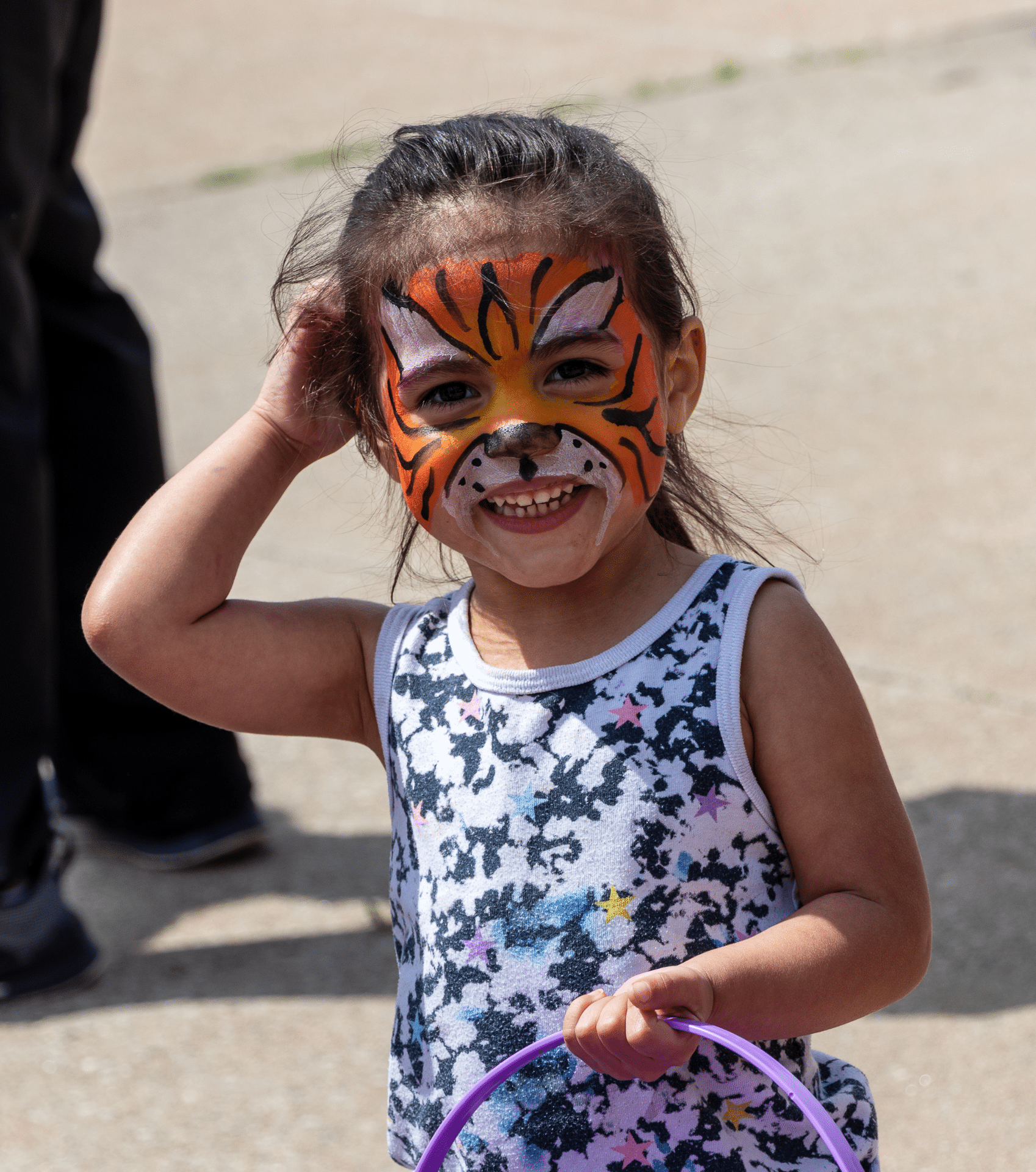 A joyful child with a tiger-painted face smiles, holding a purple hoop—celebrating community and hope together. - Muscatine Church of Christ