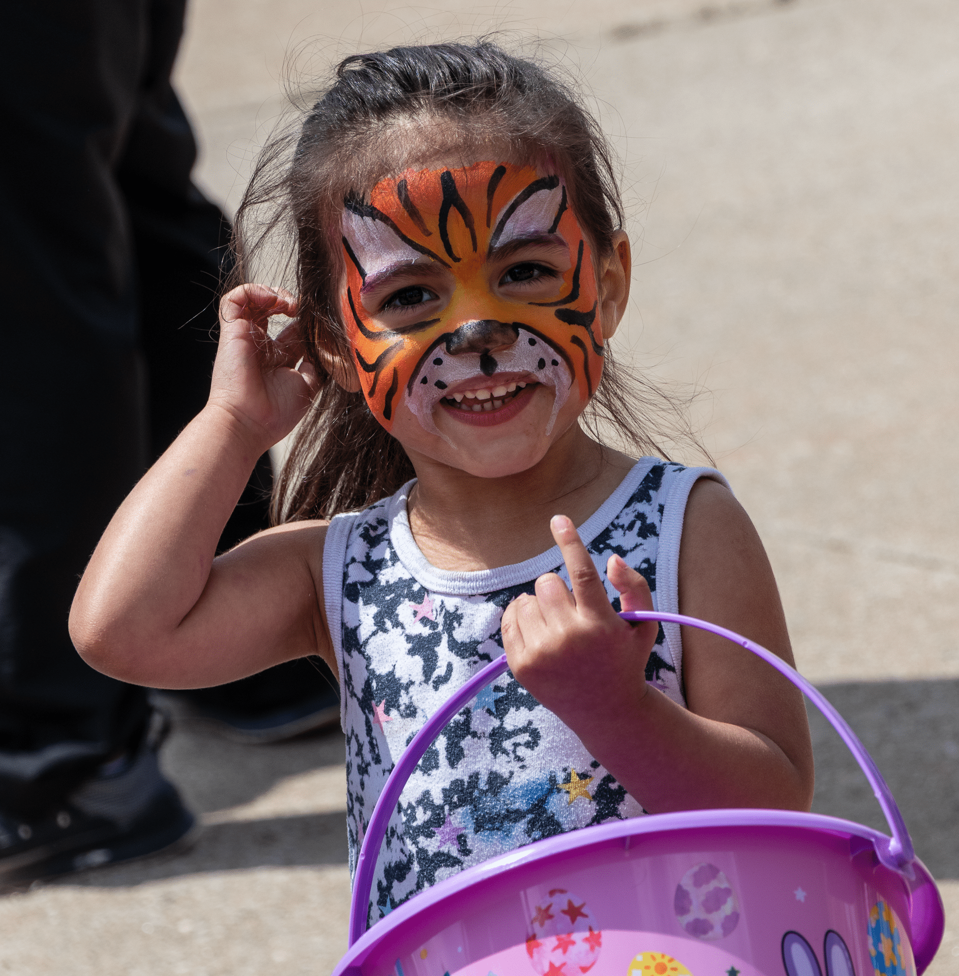 A joyful child with a tiger face paint smiles, holding a colorful bucket—celebrating hope and community together. - Muscatine Church of Christ