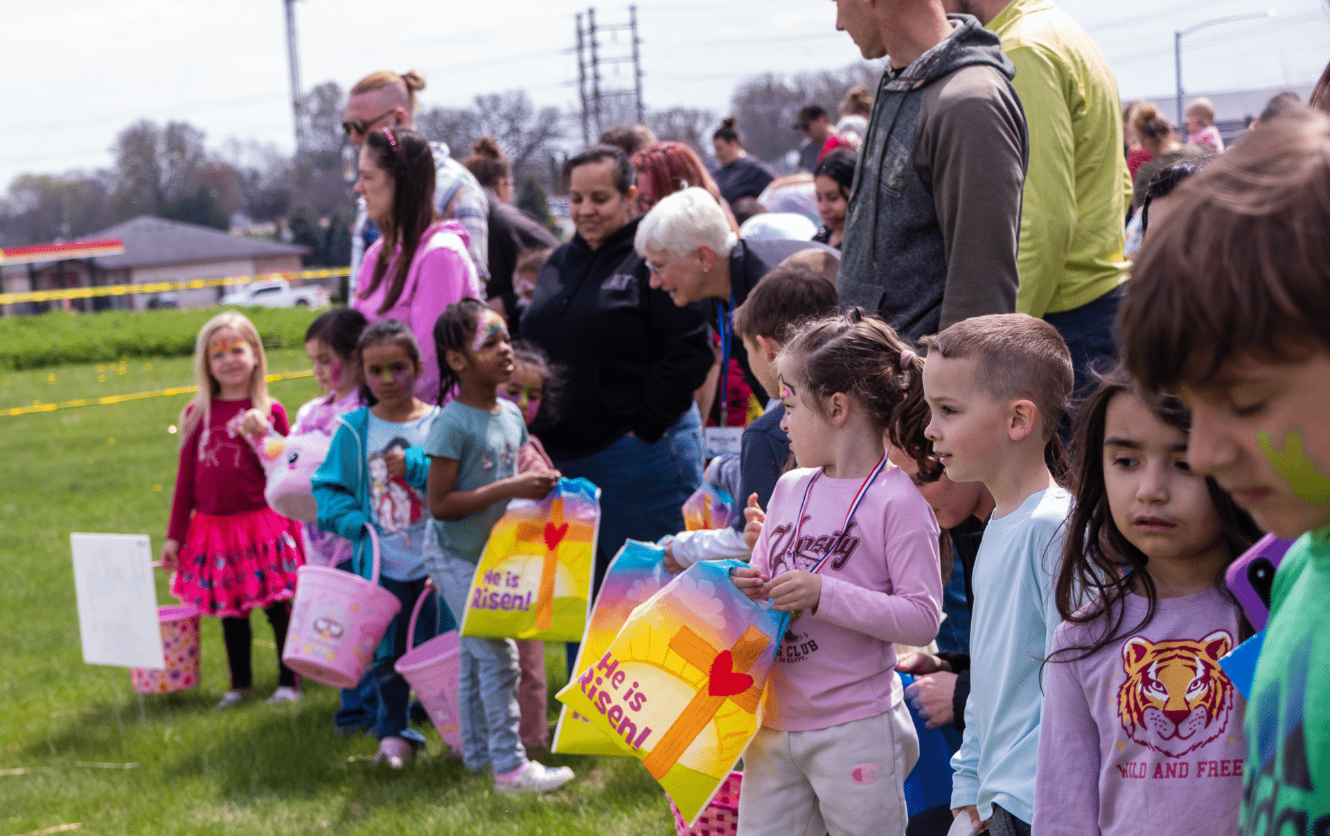 Children with bright bags line up on the grass, surrounded by caring adults—welcoming all to hope and community. - Muscatine Church of Christ
