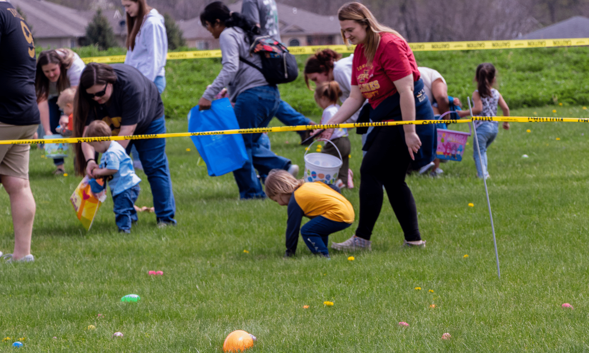 Smiling kids and adults join in a joyful outdoor egg hunt, gathering colorful eggs together on a sunny day. - Muscatine Church of Christ