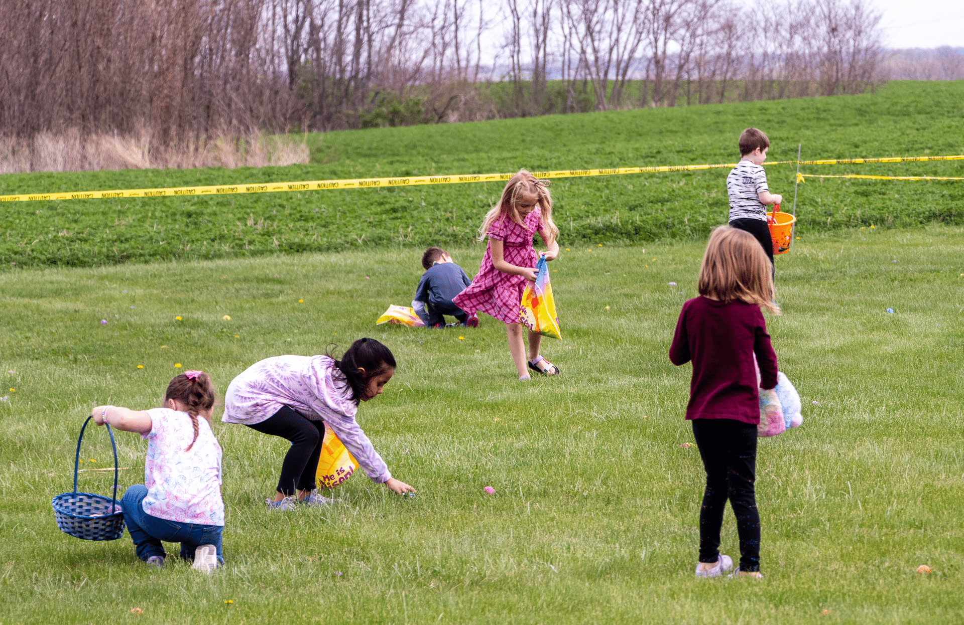 Children joyfully hunt for Easter eggs together on green grass, baskets in hand—everyone is welcome to share the hope. - Muscatine Church of Christ