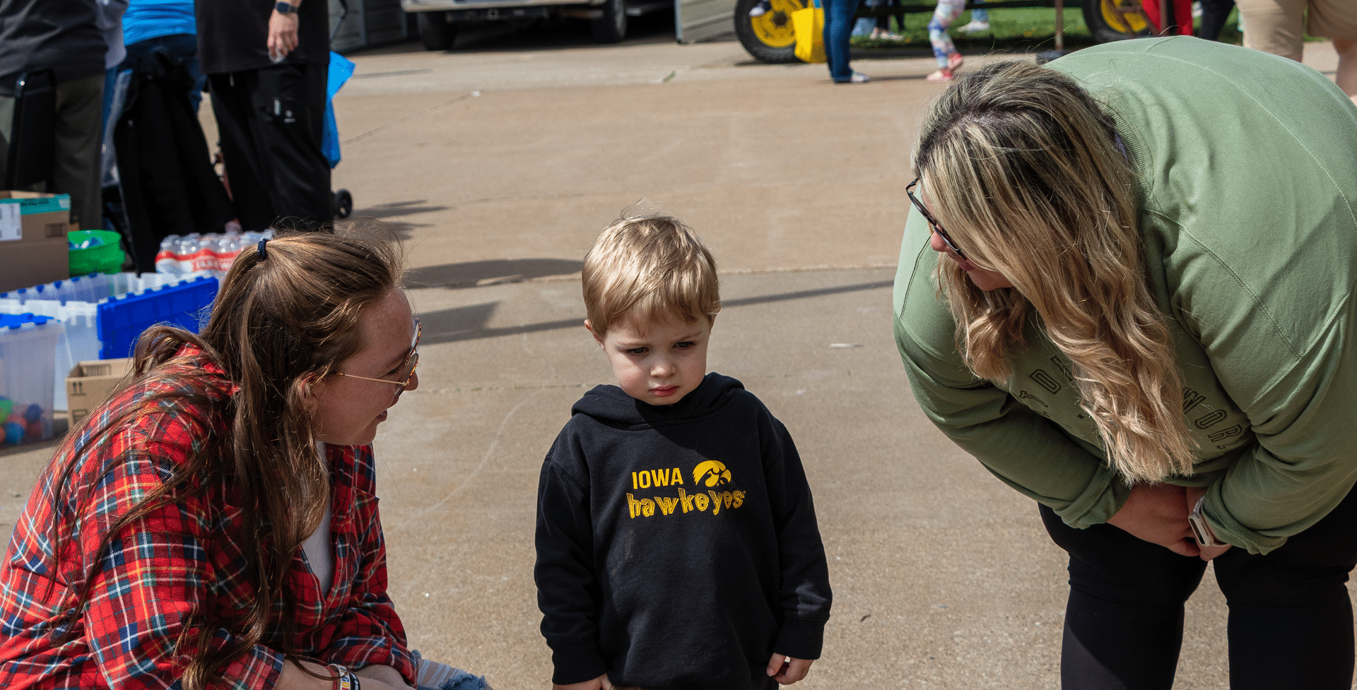 Two women warmly greet a young boy at our community event, sharing smiles, hope, and Hawkeye spirit together. - Muscatine Church of Christ