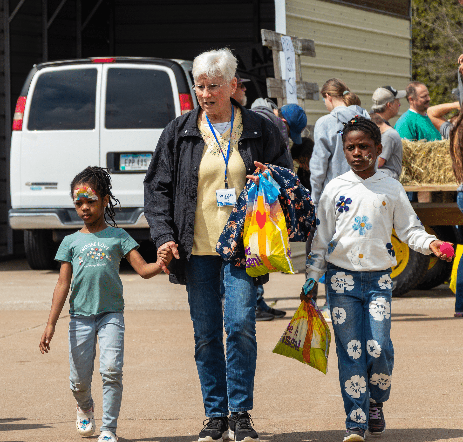 A smiling woman and two girls walk hand-in-hand with bags, surrounded by friends, sharing hope and community together. - Muscatine Church of Christ