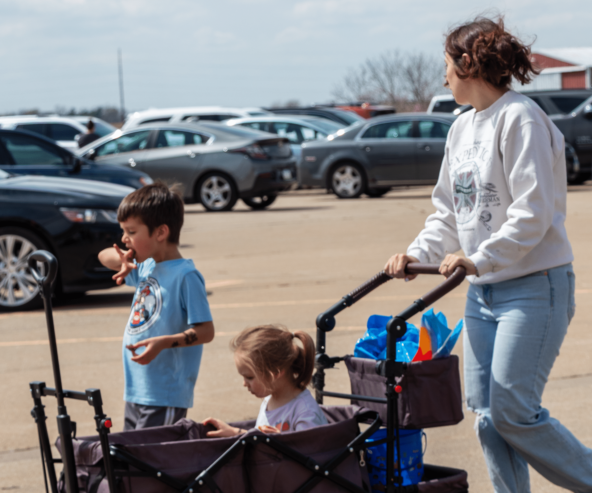 A woman joyfully guides two children in a wagon through a sunny lot, sharing smiles and hope in our caring community. - Muscatine Church of Christ