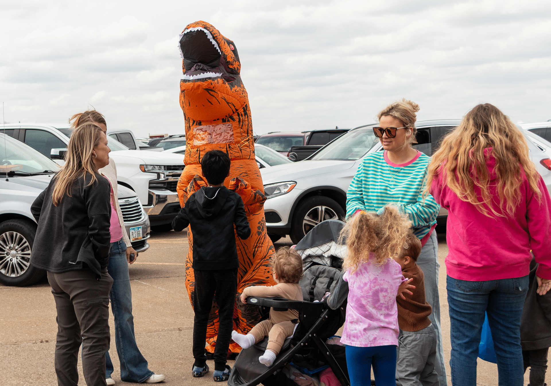 Smiling adults and kids gather outdoors with a friendly dino, sharing laughter and hope in our church family. - Muscatine Church of Christ