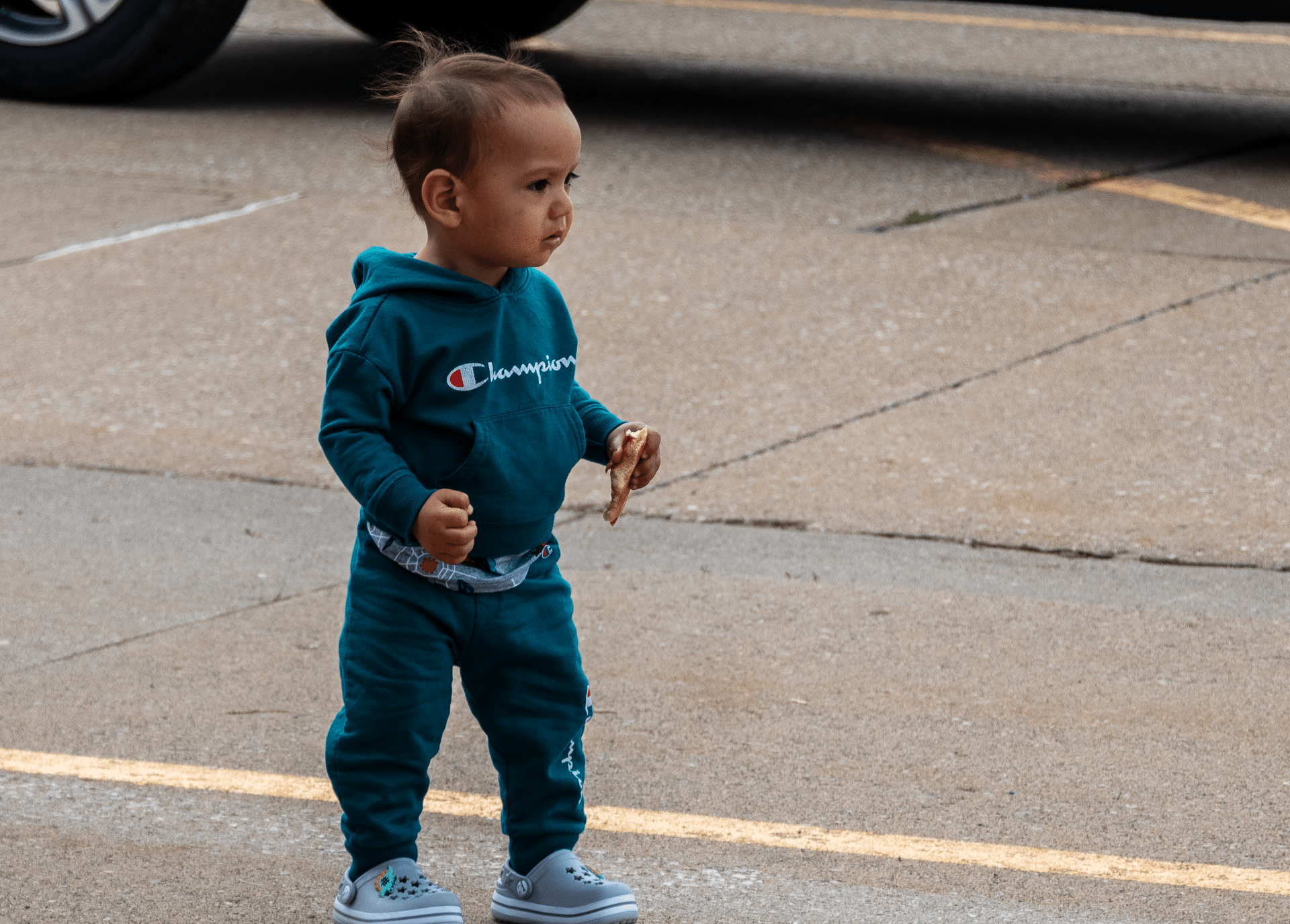 A smiling child in a teal tracksuit stands outside, welcoming all with hope and joy on a bright day. - Muscatine Church of Christ