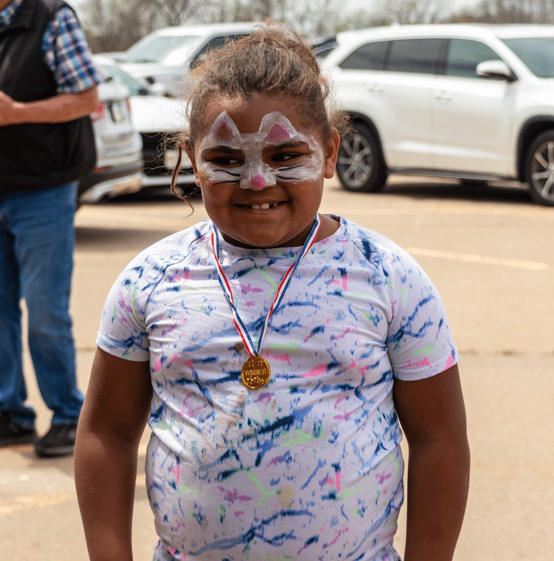 A joyful child with cat face paint and a medal smiles warmly—celebrating fun, faith, and community together. - Muscatine Church of Christ